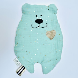 Peut inclure: Un ours en peluche bleu clair avec un cœur doré sur la poitrine. L'ours a un nez et des yeux noirs et est recouvert de paillettes dorées. L'ours a une étiquette qui dit "Camigu" dessus.