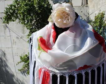 Op de afbeelding: Witte zijden sjaal met rode bloemaccenten en een delicate witte kanten rand. De sjaal is gedrapeerd over een zwarte vorm en versierd met een grote crèmekleurige roos.