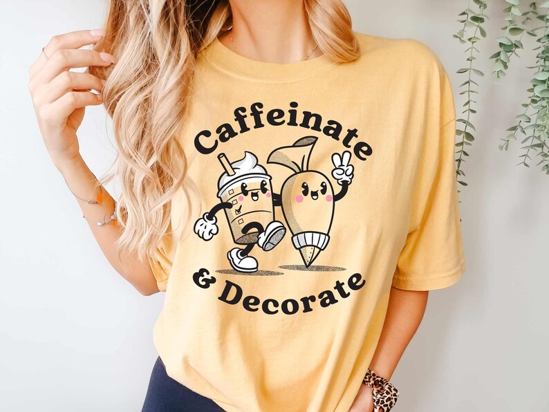 Pode incluir: Uma camiseta amarela com um gr&aacute;fico de uma x&iacute;cara de caf&eacute; e um saco de confeitar com o texto "Caffeinate & Decorate".
