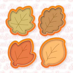 May include: A set of four leaf-shaped cookie cutters with bright orange plastic frames. Each cutter features a distinct botanical shape with embossed vein details on the interior, including a maple, an oak, and two rounded leaf designs.