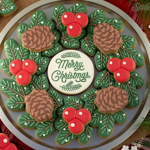 May include: A set of Christmas cookies decorated with green holly leaves, brown pine cones, and red berries. The center cookie reads "Merry Christmas" in green script.