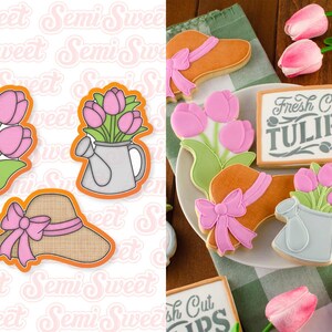 May include: Cookies in the shape of tulips, a sun hat with a pink bow, and a watering can with tulips. The cookies are decorated with pink, green, and orange icing. One cookie has a sign that says "Fresh Cut Tulips 5&cent;".