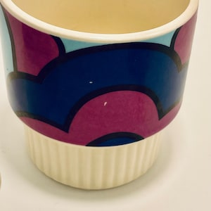 May include: A white ceramic planter with a geometric pattern in shades of pink, blue, and black. The planter has a fluted base.