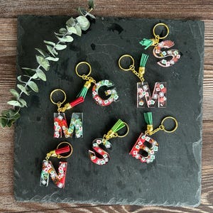 May include: A collection of letter-shaped keychains. Each keychain features a different letter, filled with a colorful design and attached to a gold keyring with a tassel. The letters are in the shape of the letters G, M, S, N, B.