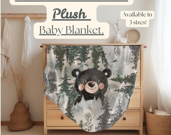 Puede incluir: Una manta de bebé de felpa con un oso negro con lunares blancos en una escena de bosque con pinos. La manta está hecha de un tejido de felpa de terciopelo suave. El texto "Woodland Bear & Pines Plush Baby Blanket. Available in 3 sizes!" está impreso en la imagen.