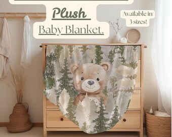 Puede incluir: Una manta de bebé de felpa con un oso marrón en una escena de bosque con pinos verdes. La manta está hecha de un tejido de felpa de terciopelo suave. El texto "Woodland Bear & Pines Plush Baby Blanket. Available in 3 sizes!" está impreso en la imagen.