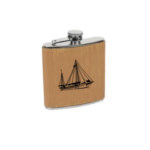 May include: A brown leather-wrapped stainless steel hip flask with a silver cap. The flask has a laser-engraved image of a sailboat.