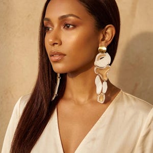 Puede incluir: Pendientes colgantes abstractos dorados y blancos. Los pendientes presentan un disco dorado en la parte superior, seguido de formas irregulares blancas y doradas. Los pendientes son largos y tienen un diseño moderno y artístico.