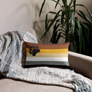 May include: A brown, beige, white, and gray throw pillow with a black bear paw print. The pillow is on a couch with a blue and white throw blanket.