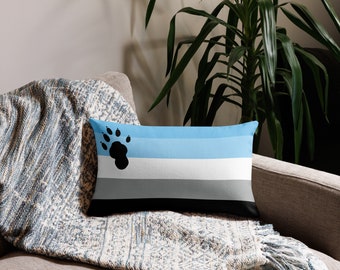 May include: A blue, white, gray, and black throw pillow with a black paw print in the top left corner. The pillow is on a couch with a blue and white throw blanket.
