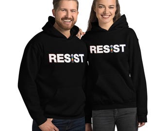 Puede incluir: Dos personas con sudaderas con capucha negras con la palabra "RESIST" impresa en blanco en la parte delantera. La palabra está estilizada con un puño levantado en colores arcoíris.