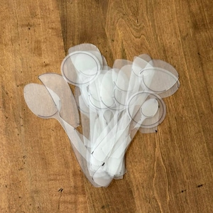May include: A stack of clear plastic spoon stencils, each with a different size and shape. The stencils are arranged in a fan shape, with the largest spoon at the top and the smallest spoon at the bottom.
