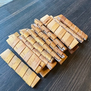 May include: A stack of handmade journals with brown paper covers and woven stitching. The journals are bound with a variety of natural materials, including bark and twine.