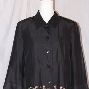 May include: A black button-down shirt with a floral embroidered trim. The embroidery is in shades of red, orange, yellow, green, and blue.
