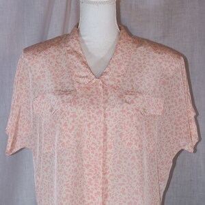 May include: A pink and white patterned short-sleeved button-up shirt with a collared neckline and two chest pockets.