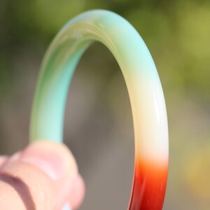 May include: A green, white, and red jade bangle bracelet. The bangle is made of smooth, polished jade and has a gradient color pattern.