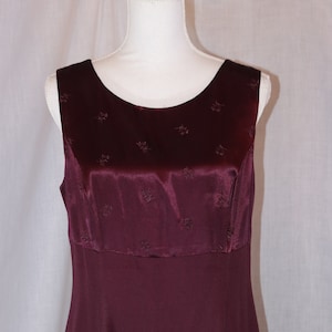 May include: A sleeveless burgundy dress with a satin bodice and a plain skirt. The bodice has a subtle floral pattern.