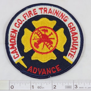 May include: A blue and yellow embroidered patch with a red fire department symbol and the text "CAMDEN CO. FIRE TRAINING GRADUATE ADVANCE".
