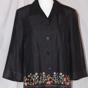 May include: A black button-down shirt with a floral embroidered trim. The embroidery is in shades of red, orange, yellow, green, and blue.