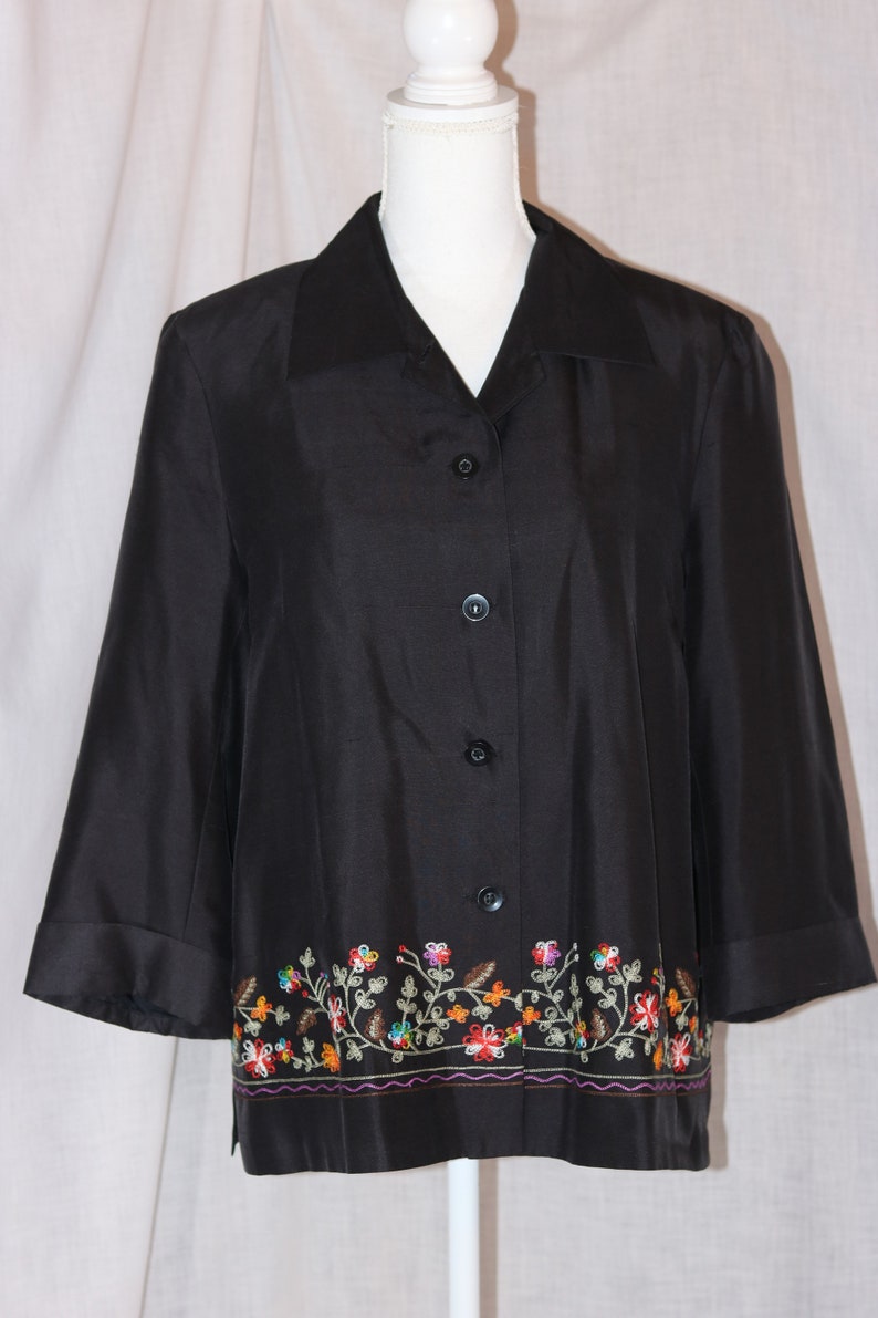 May include: A black button-down shirt with a floral embroidered trim. The embroidery is in shades of red, orange, yellow, green, and blue.
