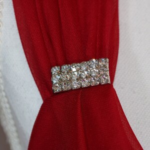 May include: A red fabric sash with a silver rhinestone embellishment.