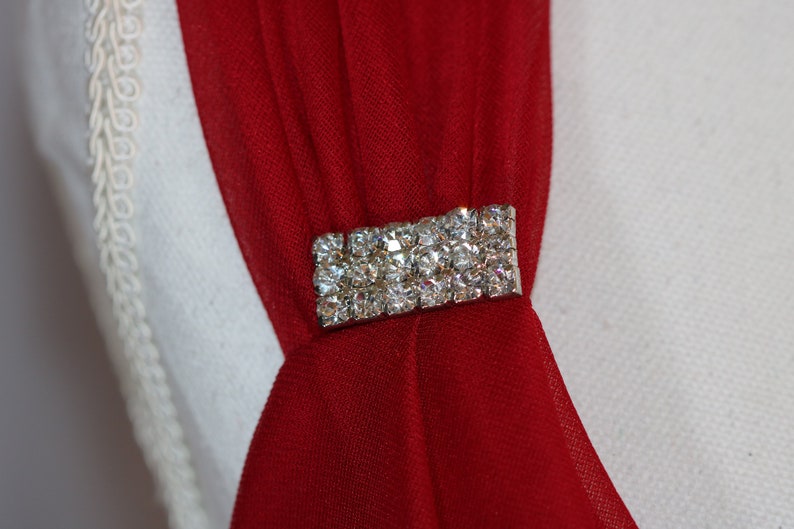 May include: A red fabric sash with a silver rhinestone embellishment.