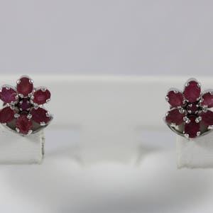 May include: A pair of silver earrings with a flower design. Each earring features a cluster of red ruby stones.