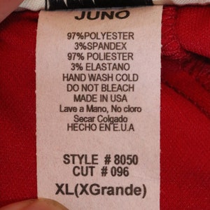 May include: A white tag with black text on a red background. The tag says "JUNO", "97% Polyester 3% Spandex", "97% Poli&eacute;ster 3% Elastano", "Hand Wash Cold", "Do Not Bleach", "Made in USA", "Lave a Mano, No cloro", "Secar Colgado", "HECHO EN E.U.A", "STYLE # 8050", "CUT # 096", and "XL(XGrande)".