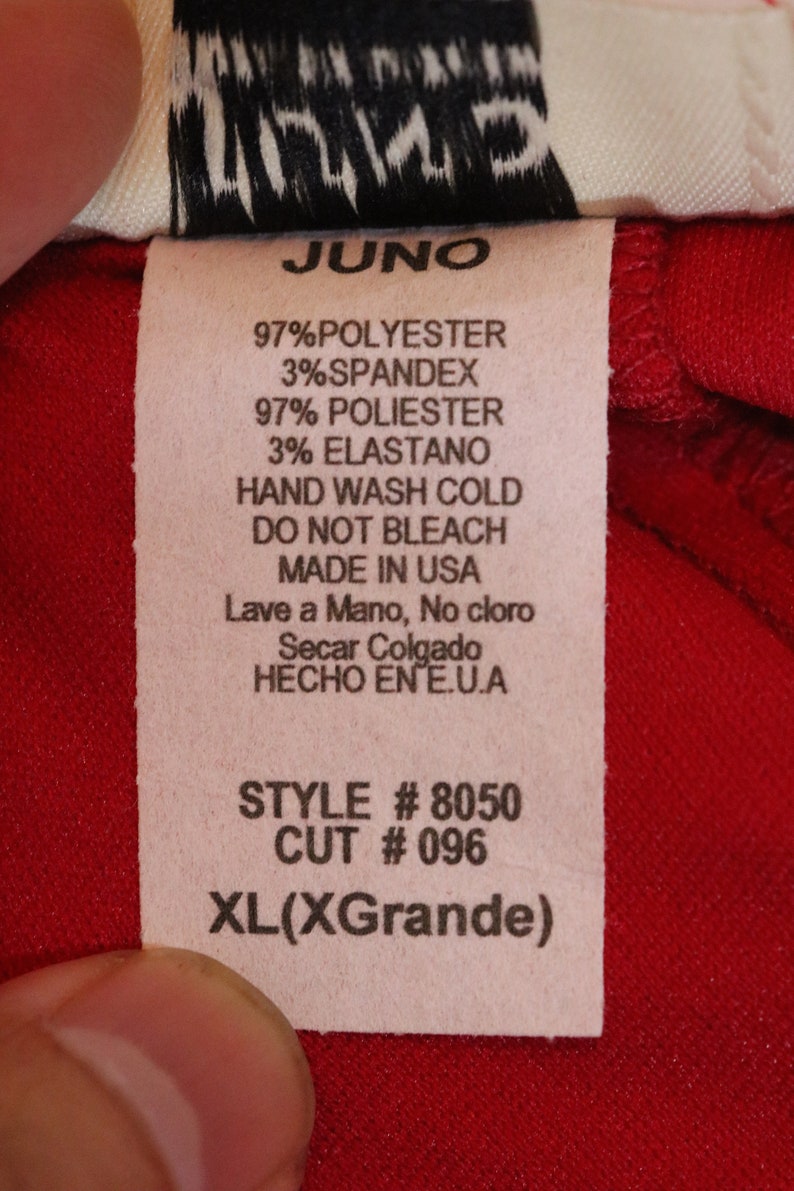 May include: A white tag with black text on a red background. The tag says "JUNO", "97% Polyester 3% Spandex", "97% Poli&eacute;ster 3% Elastano", "Hand Wash Cold", "Do Not Bleach", "Made in USA", "Lave a Mano, No cloro", "Secar Colgado", "HECHO EN E.U.A", "STYLE # 8050", "CUT # 096", and "XL(XGrande)".