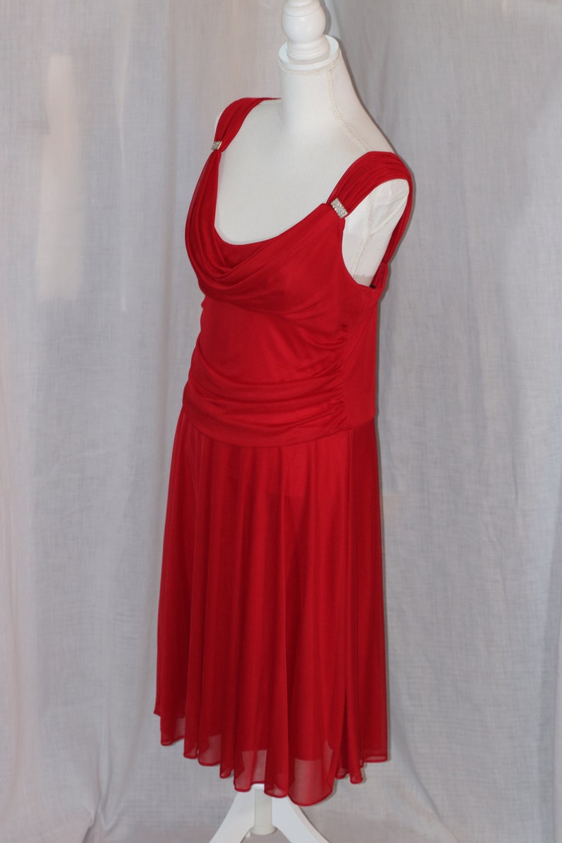 May include: A red sleeveless dress with a cowl neck and a flowing skirt. The dress has a fitted bodice and a gathered skirt. The dress is decorated with small rhinestones on the straps.