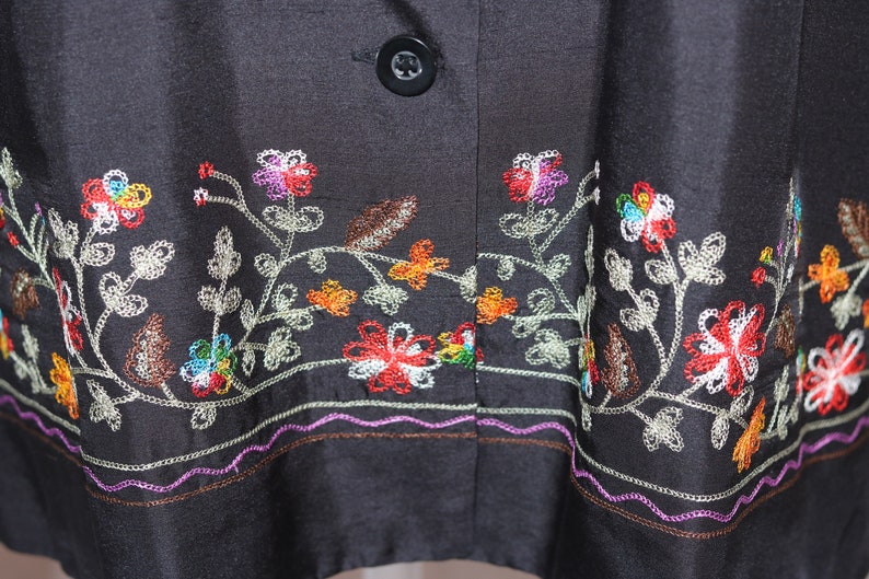 May include: Black silk jacket with colorful floral embroidery around the hem. The embroidery features a variety of flowers and leaves in shades of red, orange, yellow, green, blue, and white.