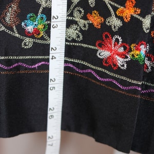 May include: Black fabric with colorful embroidered flowers and leaves. A white measuring tape is visible on the left side of the image, showing measurements in inches.