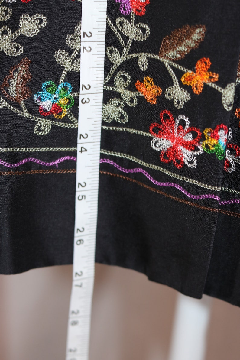 May include: Black fabric with colorful embroidered flowers and leaves. A white measuring tape is visible on the left side of the image, showing measurements in inches.