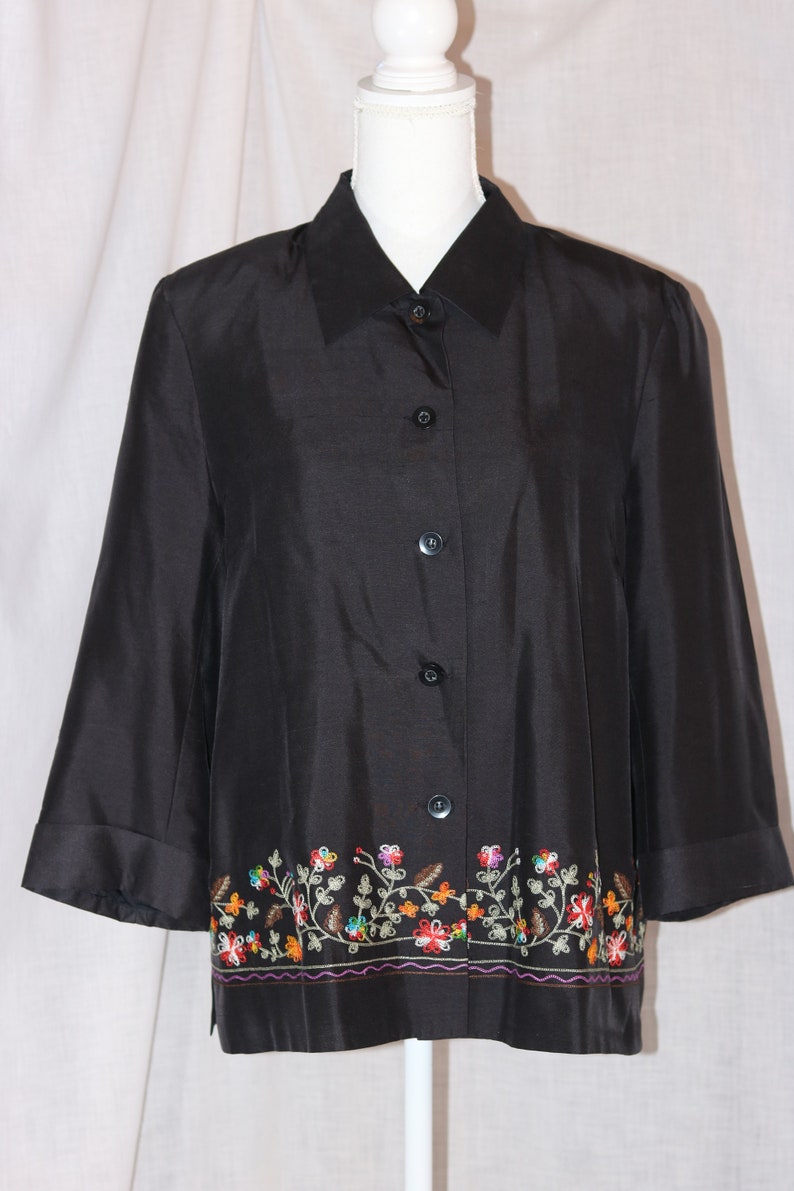 May include: A black button-down shirt with a floral embroidered trim. The embroidery is in shades of red, orange, yellow, green, and blue.