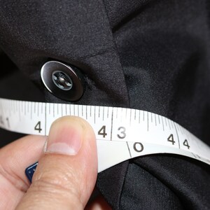 May include: A white measuring tape is wrapped around a black fabric shirt, with the numbers 4, 3, 0, and 4 visible.