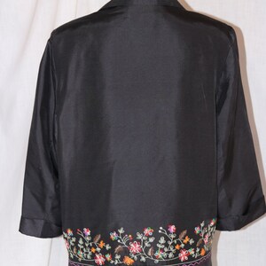 May include: A black silk jacket with a floral embroidered trim. The embroidery is in shades of red, orange, yellow, green, and purple.