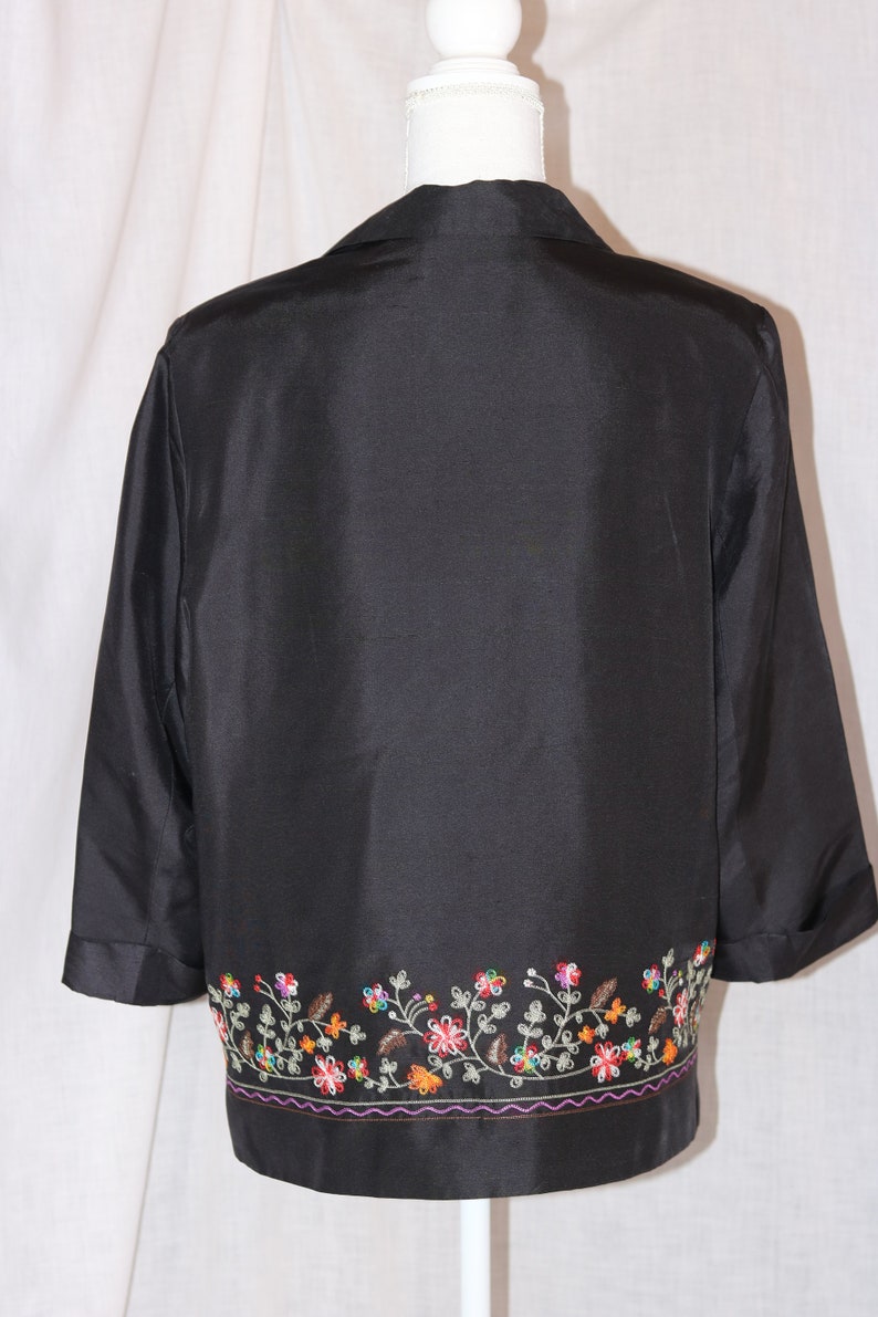 May include: A black silk jacket with a floral embroidered trim. The embroidery is in shades of red, orange, yellow, green, and purple.
