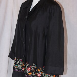 May include: A black button-down shirt with a floral embroidered trim. The embroidery is in shades of red, orange, yellow, green, and purple.