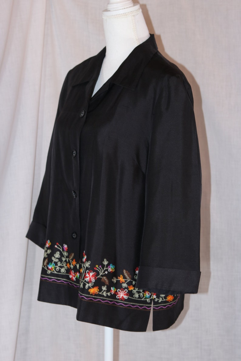 May include: A black button-down shirt with a floral embroidered trim. The embroidery is in shades of red, orange, yellow, green, and purple.