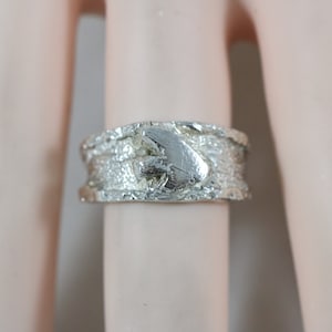 May include: A silver ring with a textured band and a raised, textured design in the center.