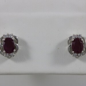 May include: A pair of silver earrings with a red oval gemstone surrounded by smaller white gemstones.