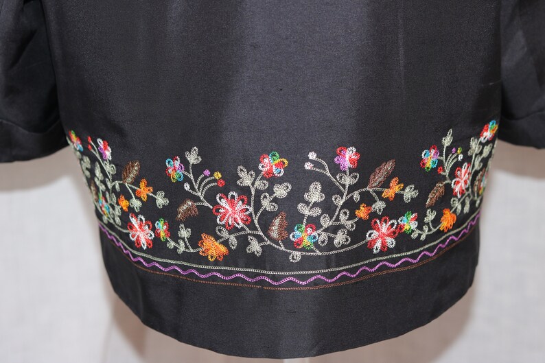 May include: Black jacket with a colorful floral embroidery design around the bottom hem.