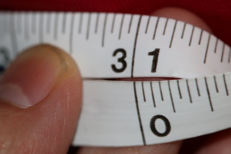May include: A white measuring tape with black markings shows the numbers 31 and 0. The tape is being held by a finger.