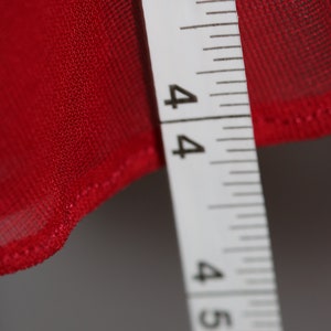May include: A close-up of a white measuring tape with black markings. The tape reads "3, 4, 4, 4, 5". The tape is measuring a red fabric.