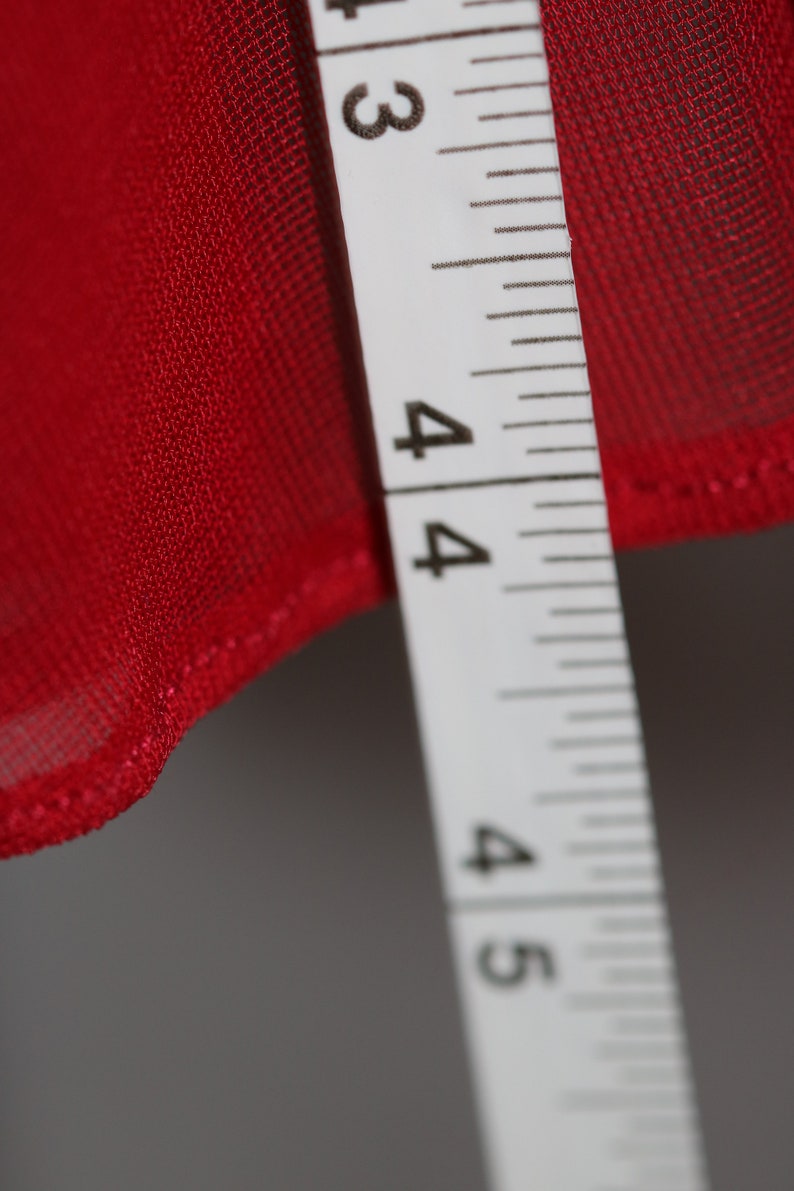 May include: A close-up of a white measuring tape with black markings. The tape reads "3, 4, 4, 4, 5". The tape is measuring a red fabric.