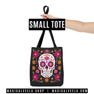 May include: Black small tote bag featuring a sugar skull design with pink, orange, and yellow floral accents. The skull has pink and purple details. The bag has black handles and the text "SMALL TOTE". The website address is also visible.