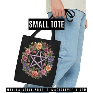Puede incluir: Una bolsa de tela negra con un pentagrama rodeado de una corona de rosas de colores. El texto "SMALL TOTE" est&aacute; impreso sobre la bolsa.
