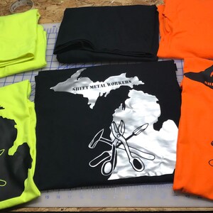 May include: Four t-shirts with a black and white outline of the state of Michigan with the text "Sheet Metal Workers" and a graphic of tools. The shirts are in the colors yellow, black, orange, and white.
