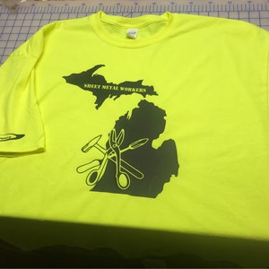 May include: A bright yellow t-shirt with a black outline of the state of Michigan. The outline includes the text "SHEET METAL WORKERS" and a graphic of tools including a hammer, pliers, and scissors.
