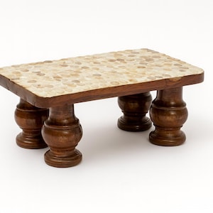 May include: A small, rectangular wooden table with a mosaic tile top. The table has four turned legs and a dark brown finish. The mosaic top is composed of small, light-colored stones. The table is approximately 12 inches long, 8 inches wide, and 6 inches tall.